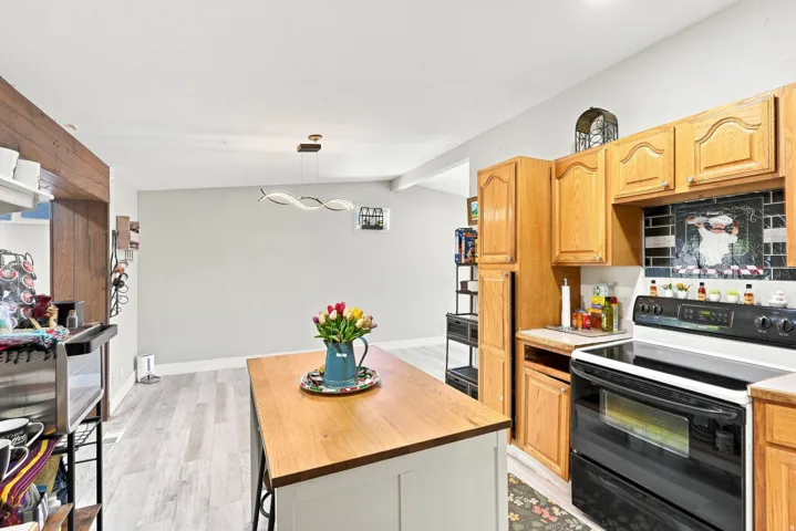 Wood-finish flooring throughout, wood-look accent wall, modern pendant lighting, wood cabinetry, and a tile backsplash