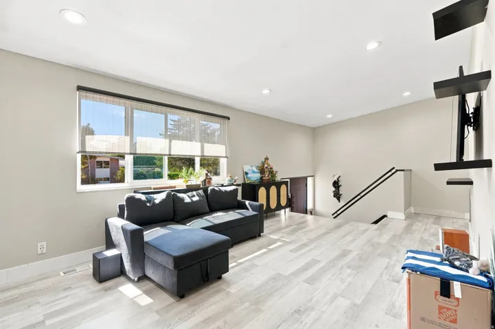Recessed lighting, light wood-finish flooring, staircase with dark handrails, built-in shelving, and large windows with blinds