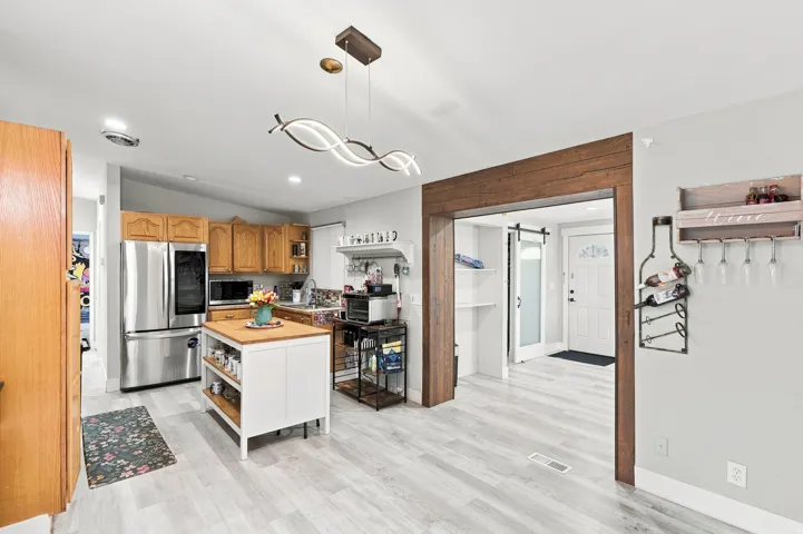 Wood-finish flooring throughout, stainless steel refrigerator, wood cabinetry, and a decorative wood-wrapped entryway