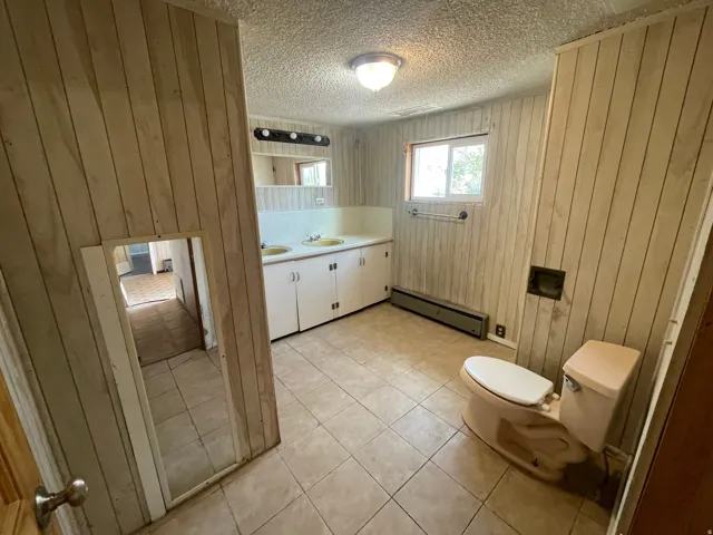 Tiled flooring, dual sink vanity, wall paneling, built-in cabinetry, and a window for natural light