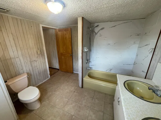 Tiled flooring with an integrated toilet, a bathtub with a tiled surround, and a vanity with a drop-in sink