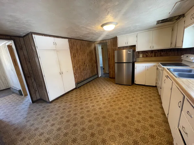 Kitchen featuring wood-panel walls, patterned flooring, white cabinetry, and a stainless steel refrigerator