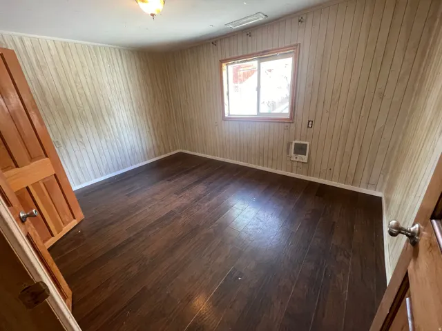 Wood-finish flooring with paneling walls, natural wood trim window, and built-in wall heater