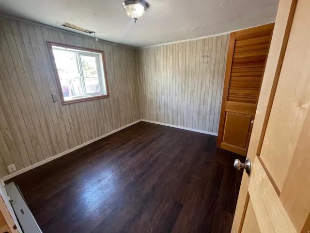 Wood-finish flooring, wood panel walls, a single window with wood trim, and a wood louvered door