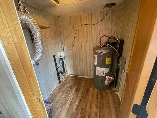Wood-finish flooring, paneled walls, water heater, utility connections, and exposed ductwork