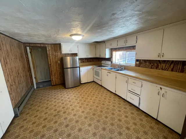 Kitchen featuring wood-panel walls, white cabinetry, a stainless steel refrigerator, and patterned flooring