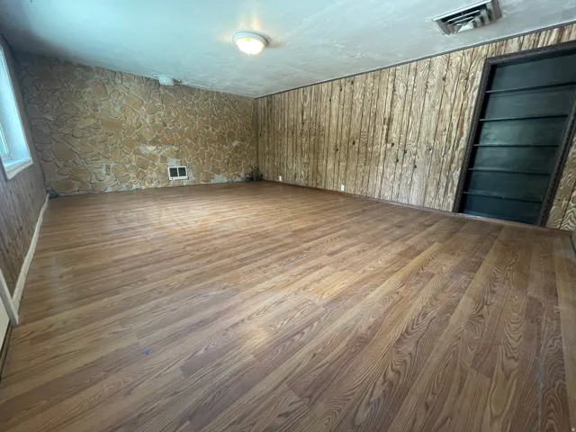 Wood-finish flooring throughout, featuring a stone-clad accent wall, paneled wall finishes, and an integrated wall-mounted bookshelf