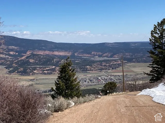 Expansive mountain landscape with distant town, visible from a natural dirt path