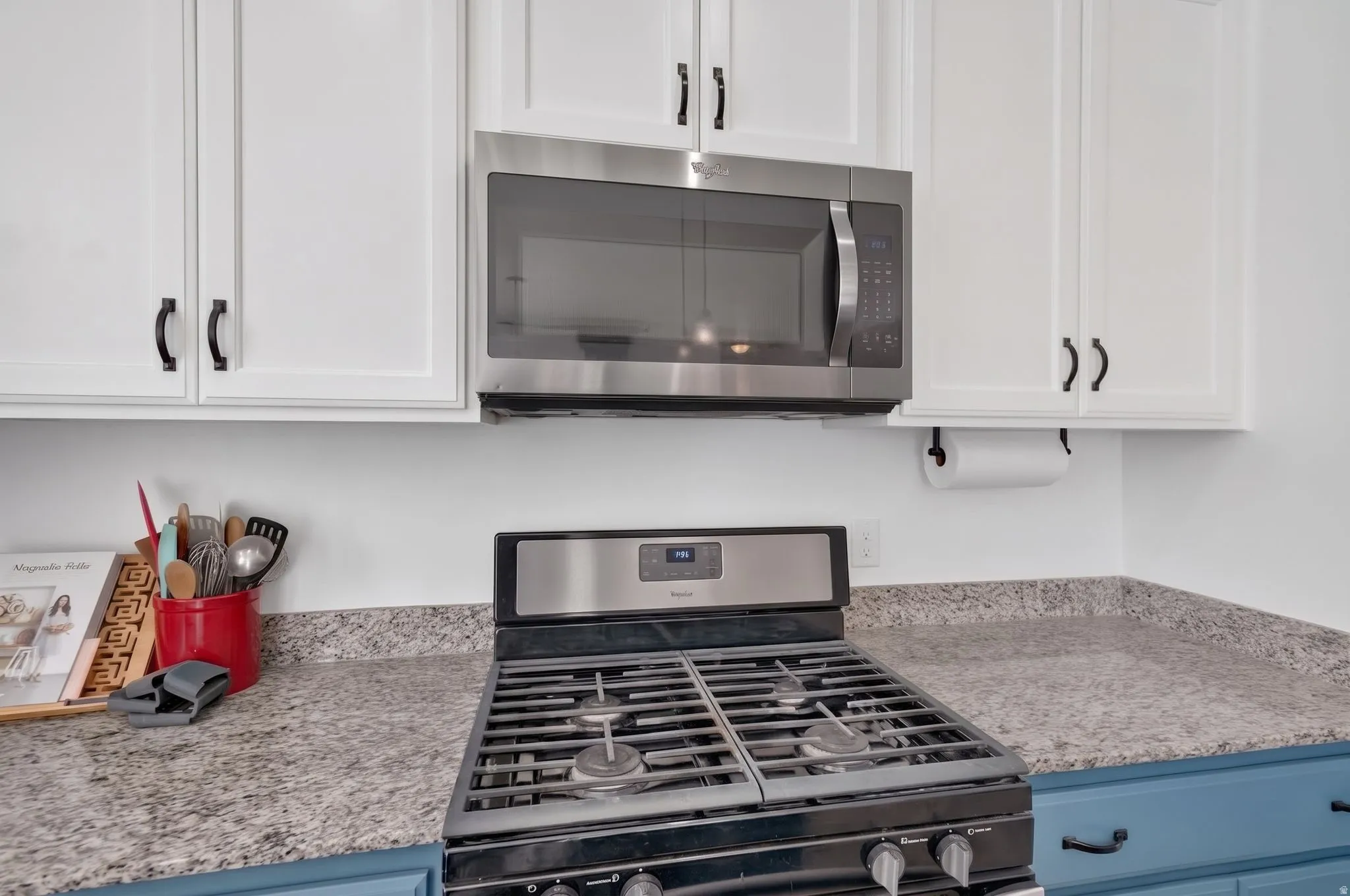 White upper cabinetry with black hardware, stainless steel microwave, gas range, and speckled countertops
