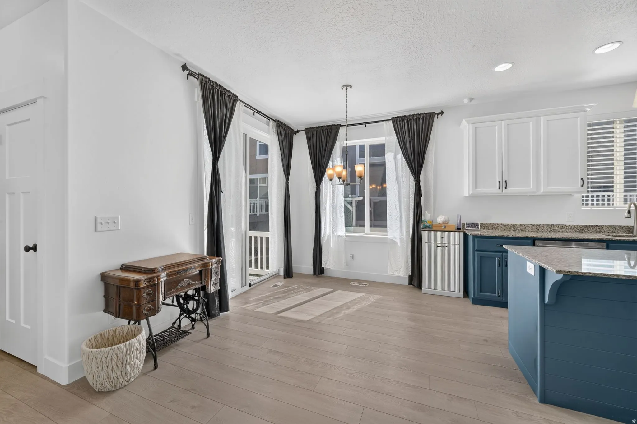 Light wood-finish flooring throughout, white shaker-style upper cabinetry, deep blue lower cabinetry, granite countertops, and a modern chandelier