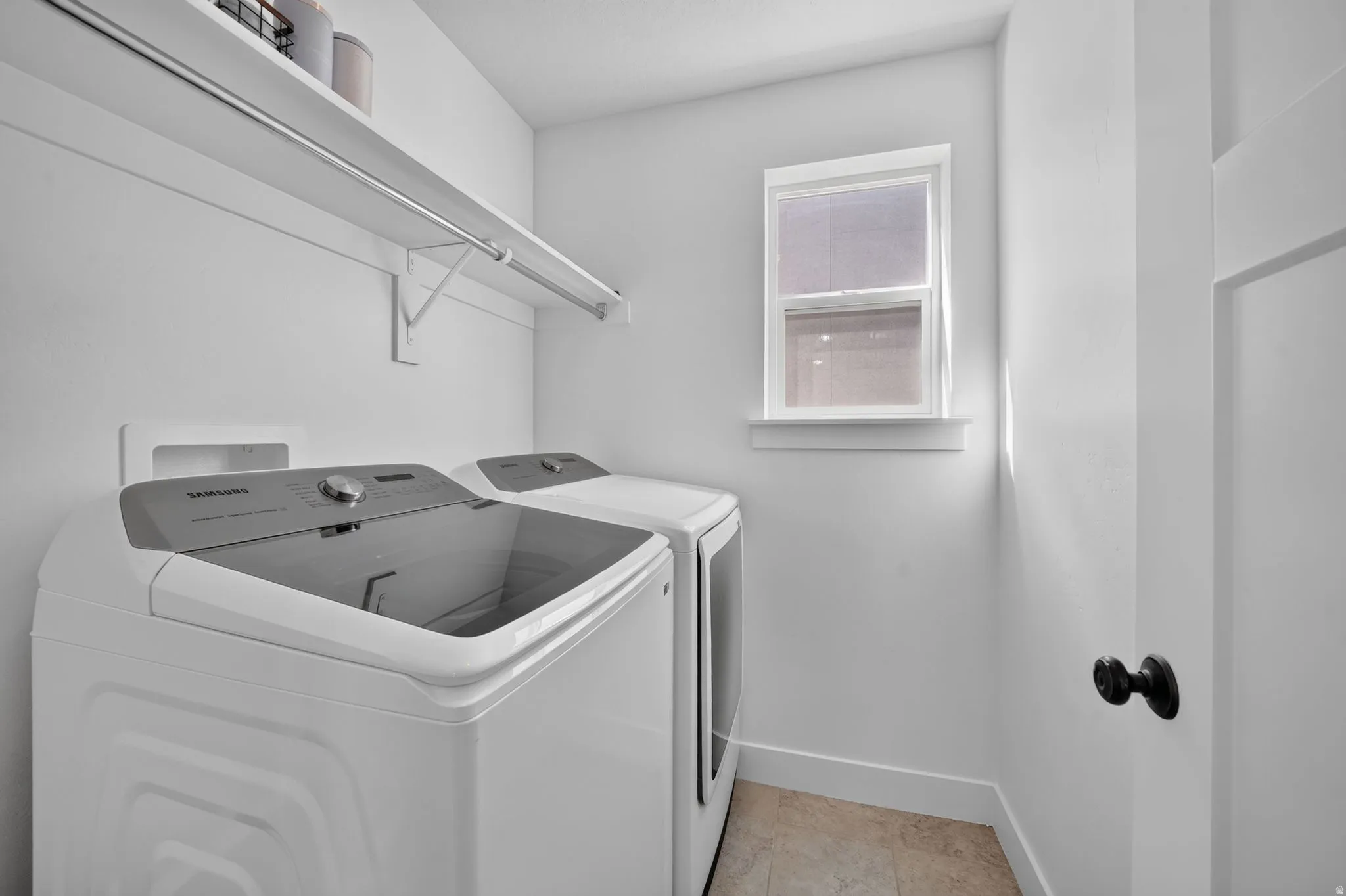 Utility room featuring white walls, a single window, an overhead shelf, a hanging rod, and light-toned floor tiling