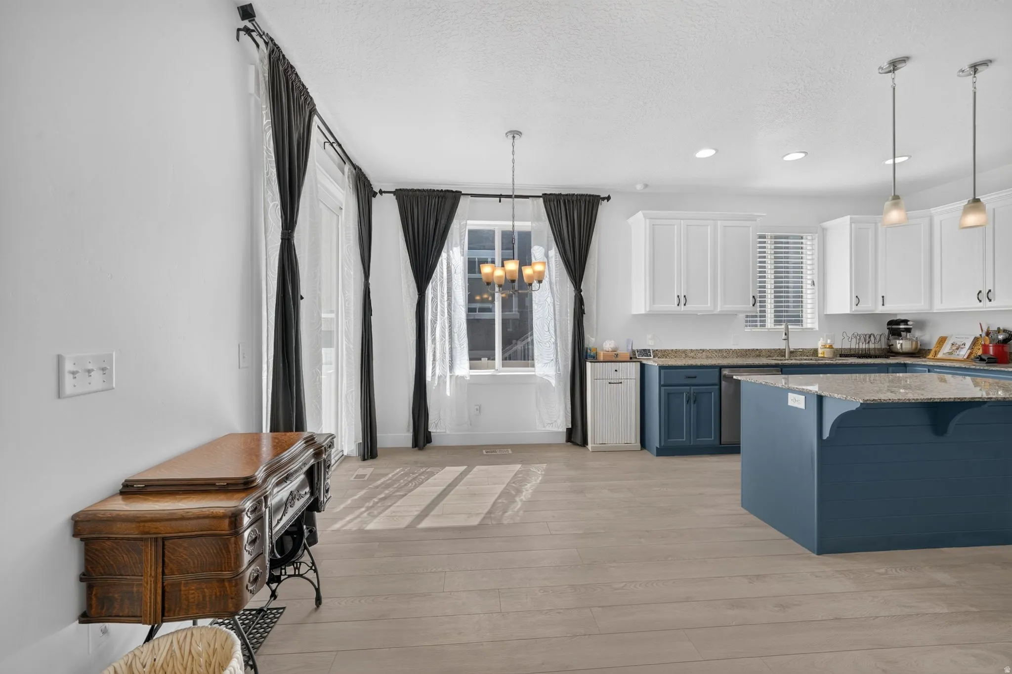 Wood-finish flooring, white cabinetry, blue island, granite countertops, and recessed lighting