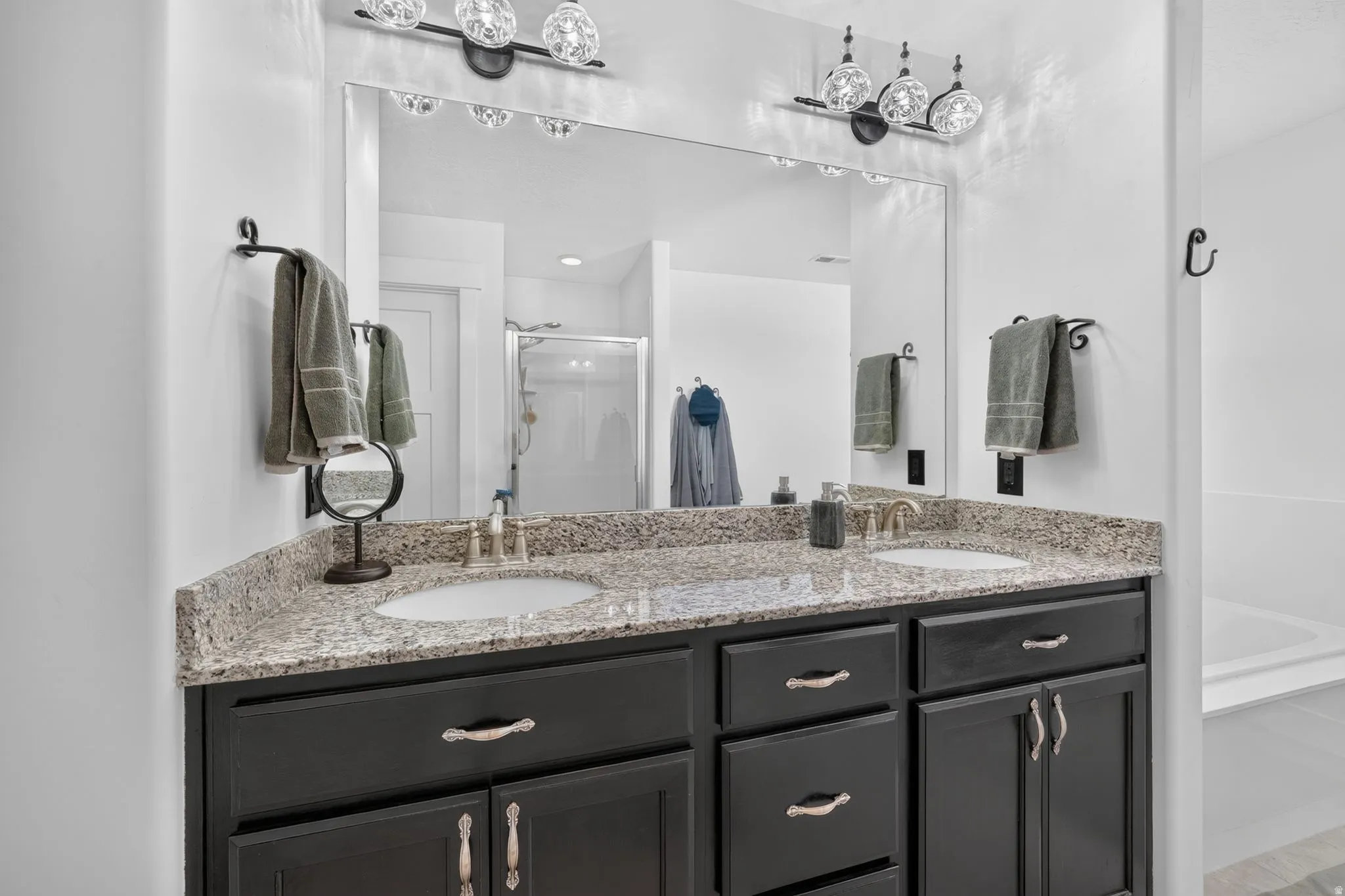 Dual undermount sinks with brushed nickel fixtures, granite-style countertop, dark wood-finish cabinetry, and decorative overhead lighting