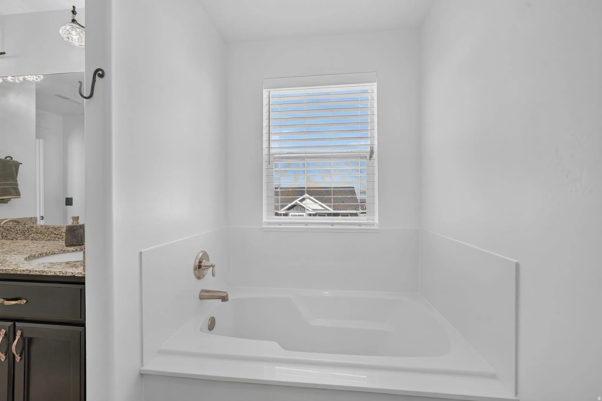 White built-in bathtub with brushed nickel fixtures and a window with blinds