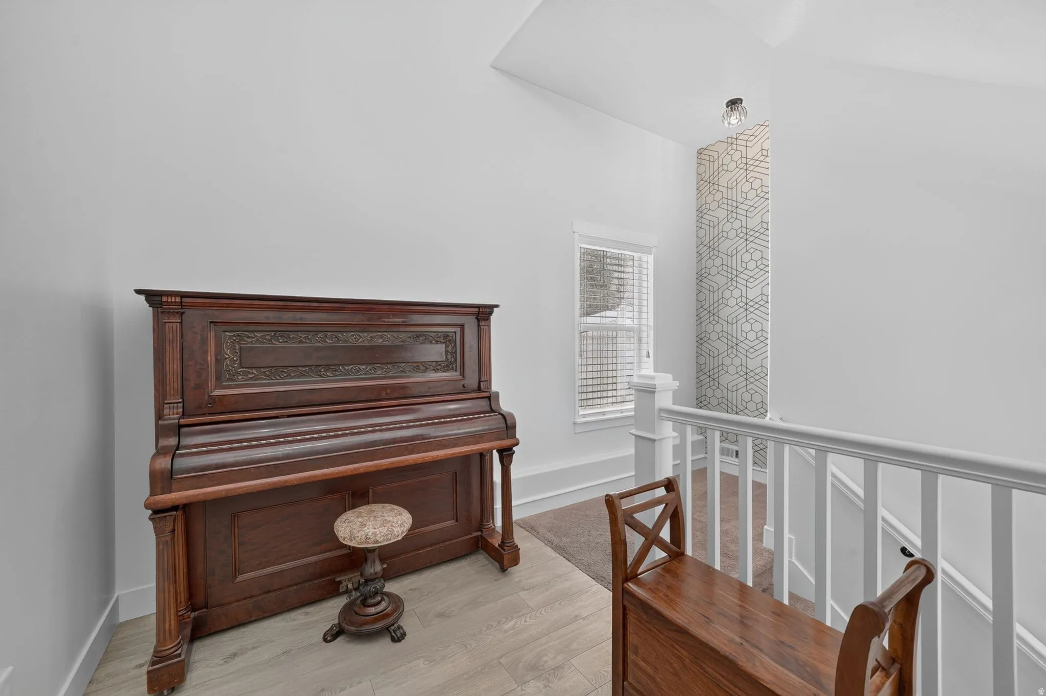 Vaulted ceiling with an accent wall, window with horizontal blinds, light wood-finish flooring, and white railing