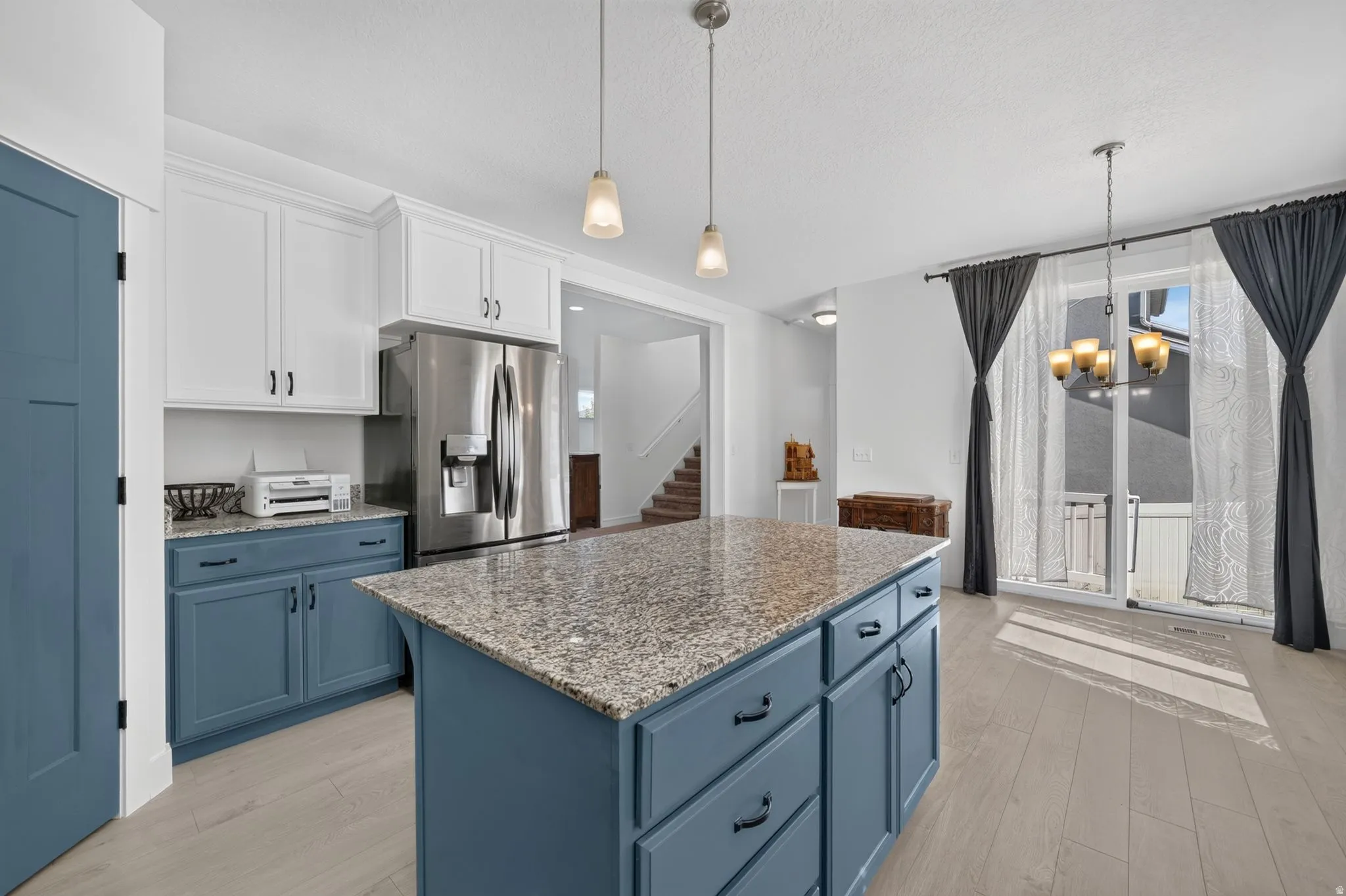 Kitchen featuring a granite-top island, stainless steel refrigerator, two-tone cabinetry, wood-finish flooring, and a sliding glass door