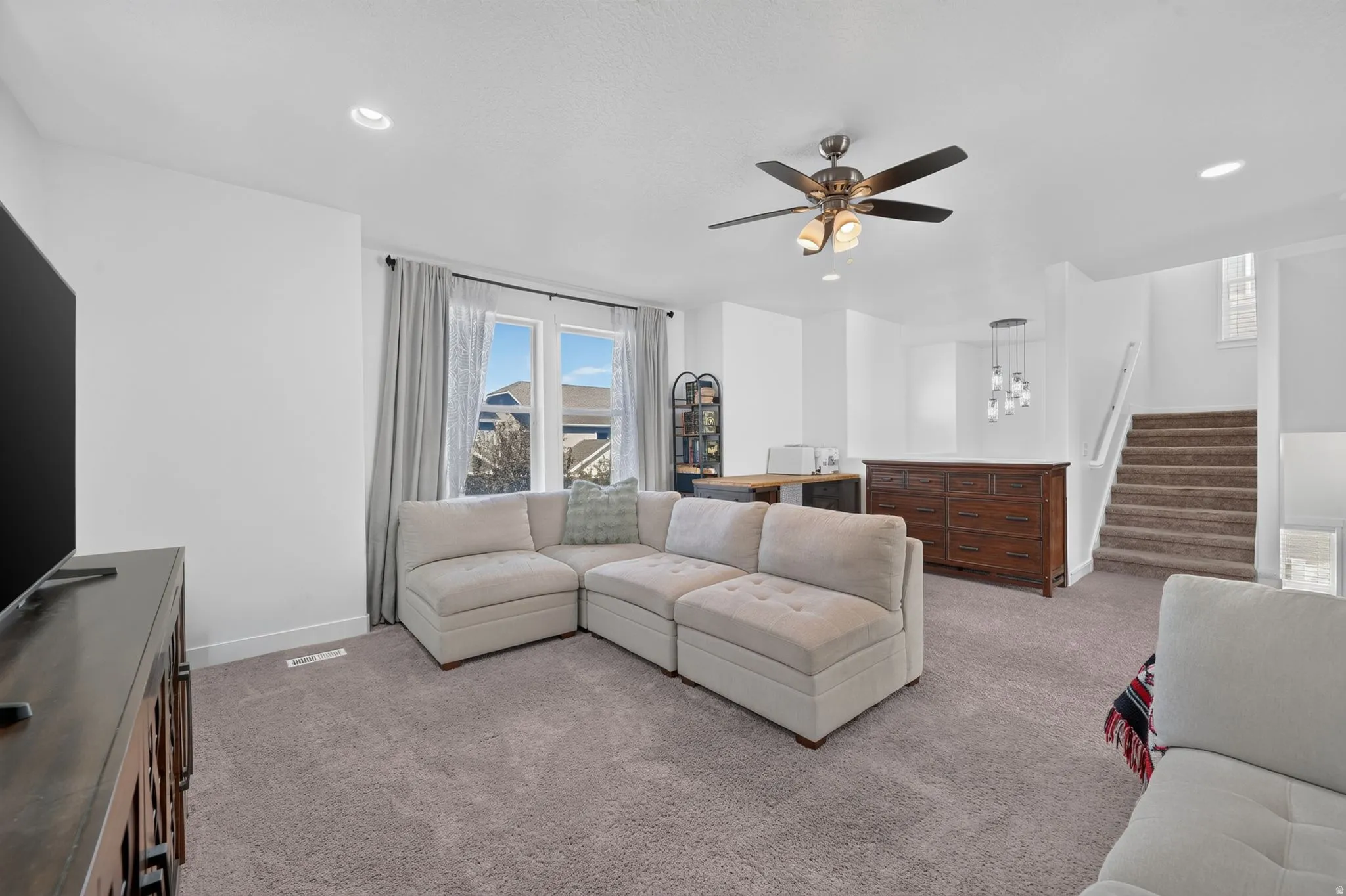 Carpeted living area featuring recessed lighting, a ceiling fan, a large window, and a carpeted staircase with white railings