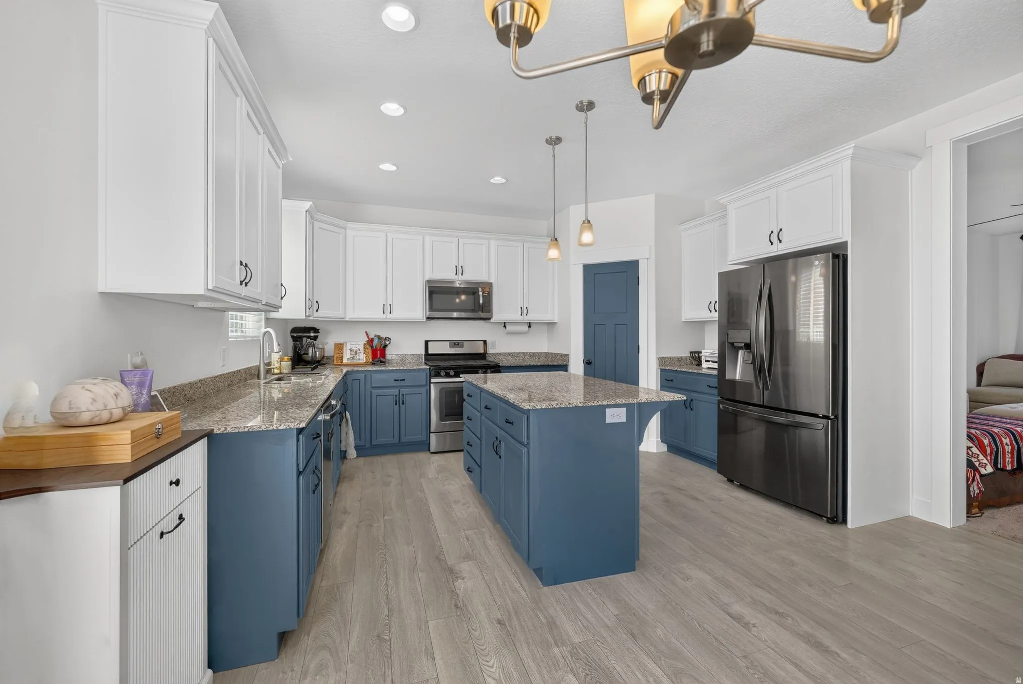 Kitchen featuring a central island, two-tone cabinetry, stainless steel appliances, granite countertops, and wood-finish flooring