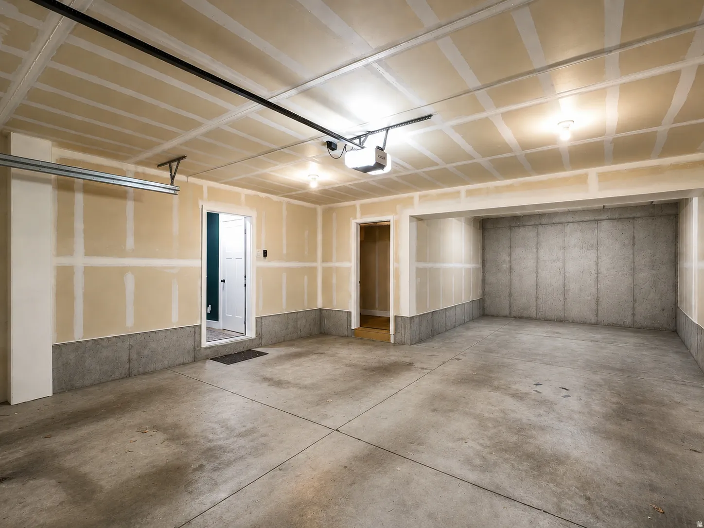 Spacious garage with concrete flooring, exposed drywall, overhead lighting, and an automatic garage door opener