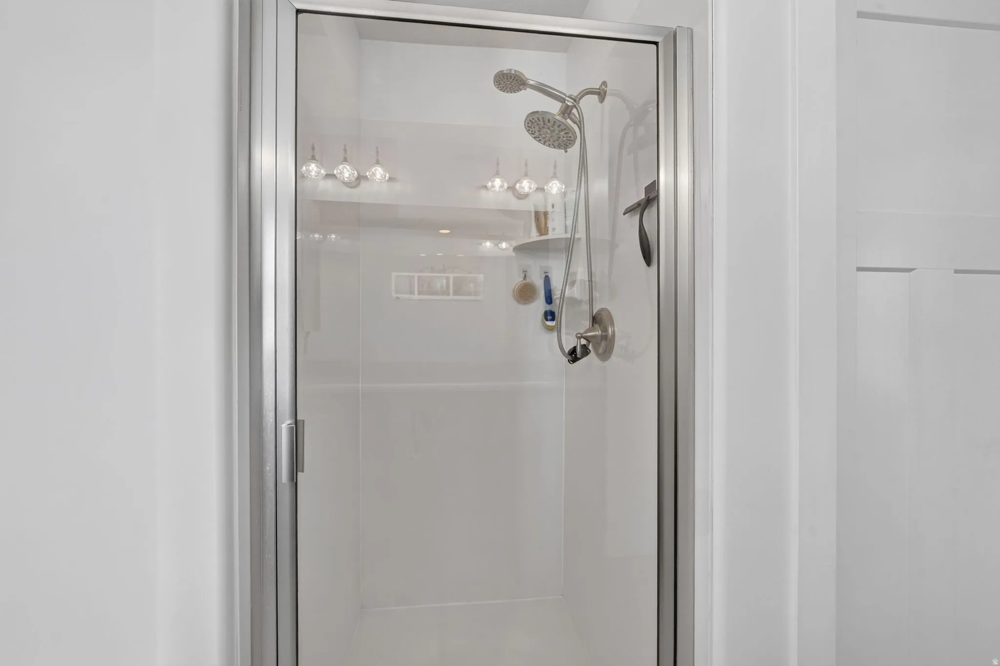 Glass-enclosed shower with brushed nickel fixtures and a built-in shelf