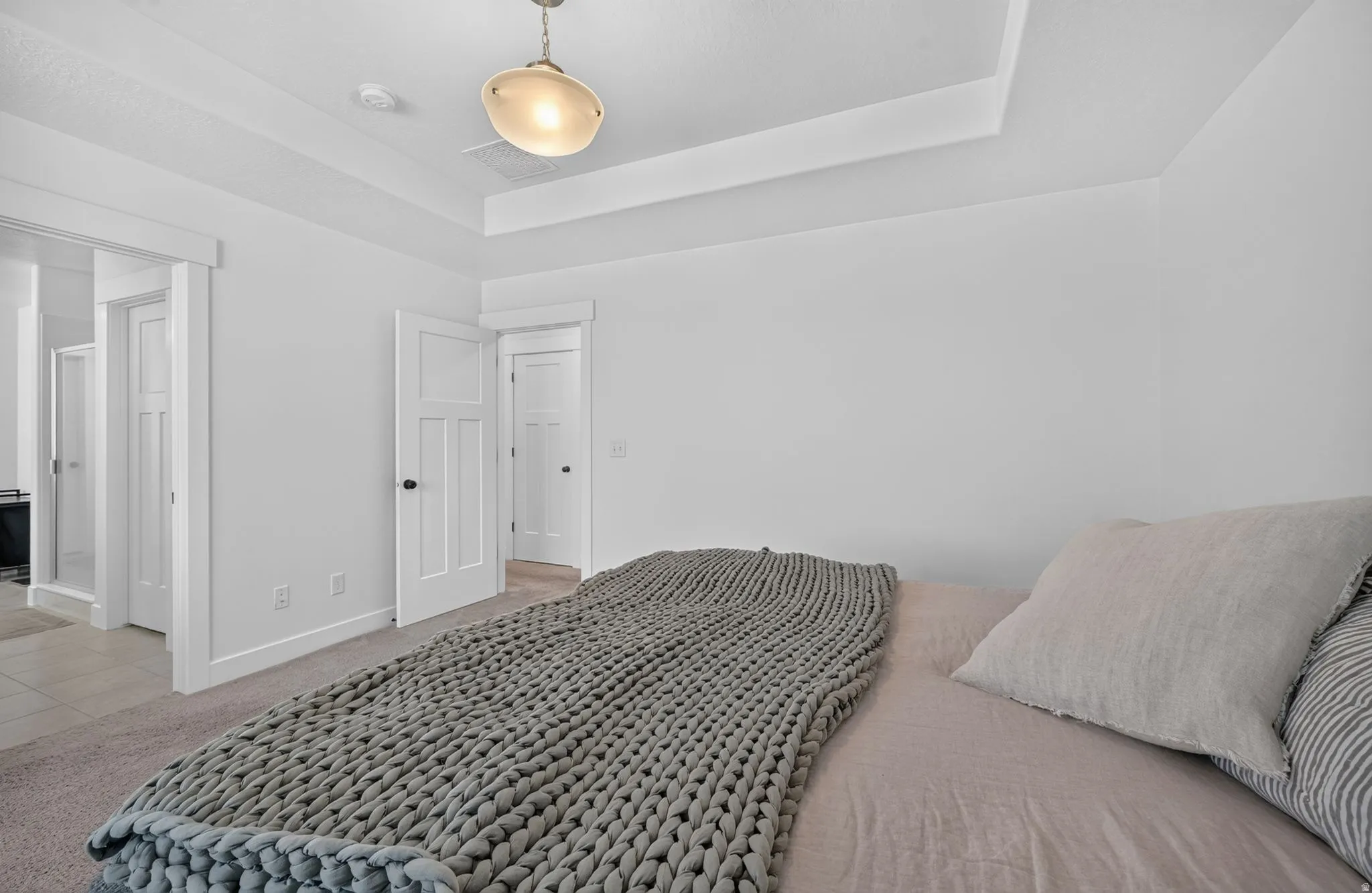 Recessed tray ceiling, neutral carpet flooring, modern pendant light fixture, three-panel interior doors, and white trim throughout