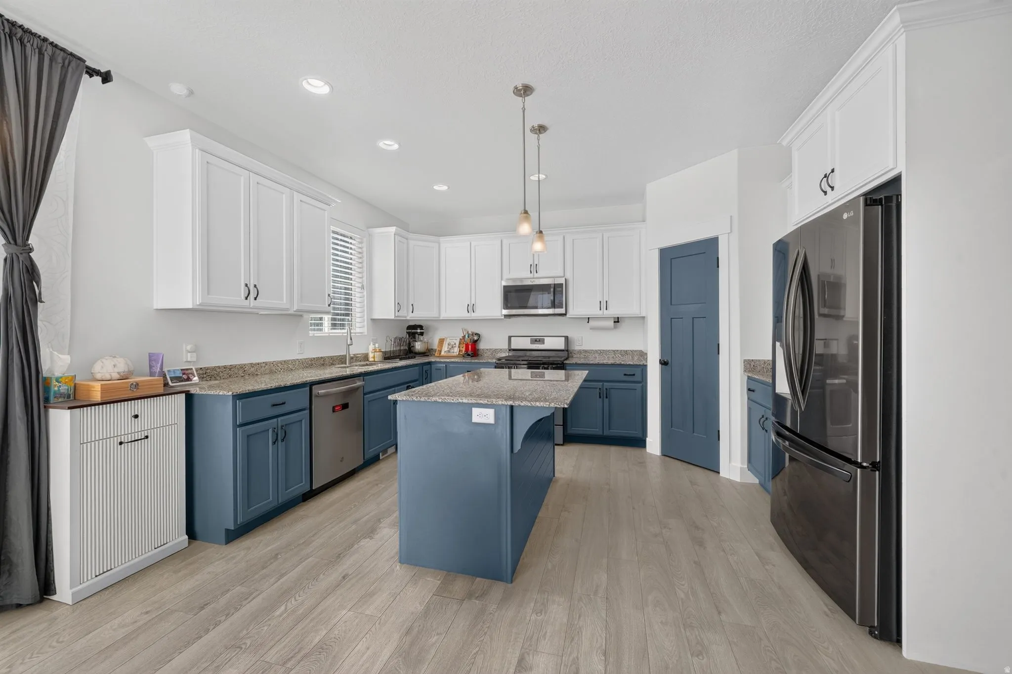 Kitchen featuring two-tone cabinetry, a central island with countertop, stainless steel appliances, pendant lighting, and wood-finish flooring
