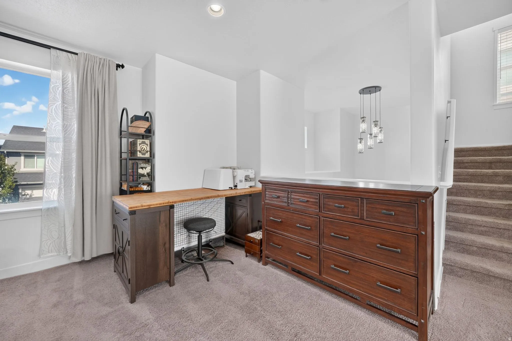 Carpeted landing featuring a built-in desk, window with roller shades, and a multi-pendant light fixture