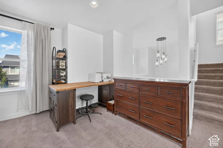 Carpeted landing featuring a built-in desk, window with roller shades, and a multi-pendant light fixture