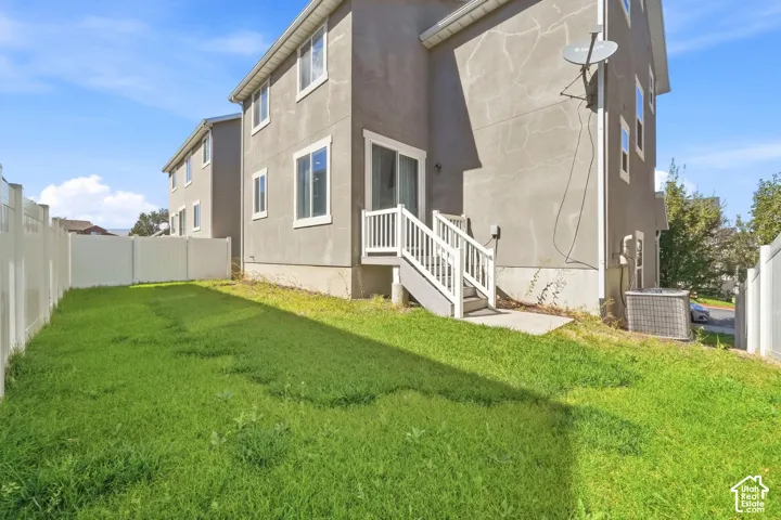 Private backyard with a full vinyl fence, grass lawn, ground-level patio, and exterior stairs leading to a sliding glass door
