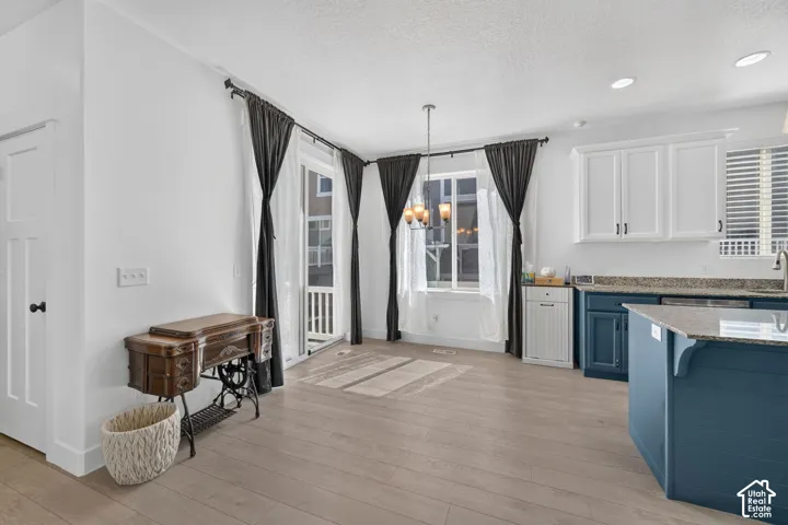 Light wood-finish flooring throughout, white shaker-style upper cabinetry, deep blue lower cabinetry, granite countertops, and a modern chandelier