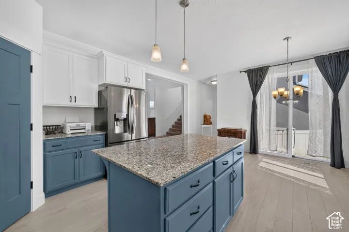 Kitchen featuring a granite-top island, stainless steel refrigerator, two-tone cabinetry, wood-finish flooring, and a sliding glass door