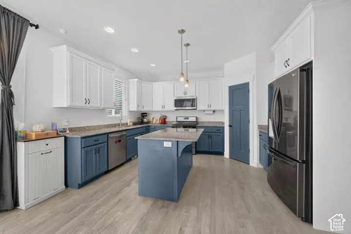 Kitchen featuring two-tone cabinetry, a central island with countertop, stainless steel appliances, pendant lighting, and wood-finish flooring