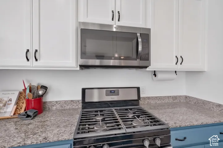 White upper cabinetry with black hardware, stainless steel microwave, gas range, and speckled countertops