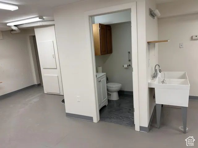 Room with painted walls, multiple overhead lighting fixtures, and light gray flooring and entrance to basement bathroom