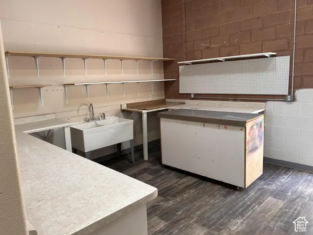 Back room - utility sink with dual basins, LVP wood-finish flooring, brick wall accent, built-in shelving, and countertop space