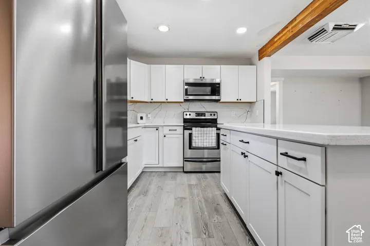Modern kitchen featuring white shaker cabinetry, stainless steel appliances, light-toned stone countertops, and wood-finish flooring