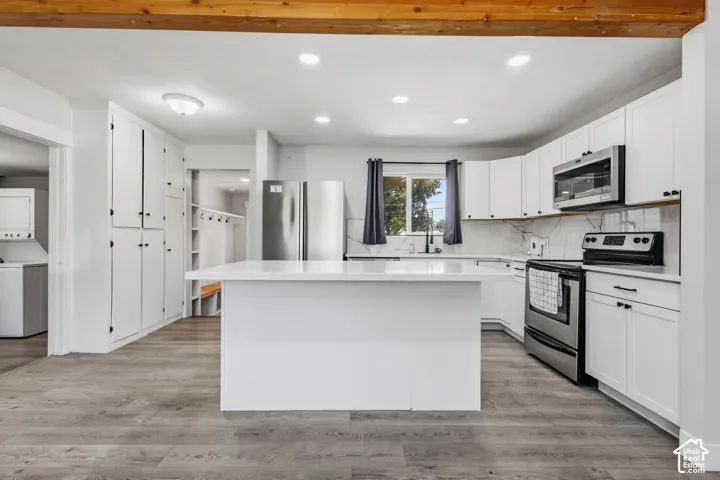 Bright kitchen featuring a substantial island, stainless steel appliances, extensive white cabinetry, a decorative backsplash, and wood-finish flooring