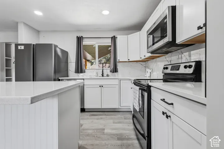 Kitchen featuring an expansive island, white shaker cabinetry, white countertops, and a white marble-finish backsplash