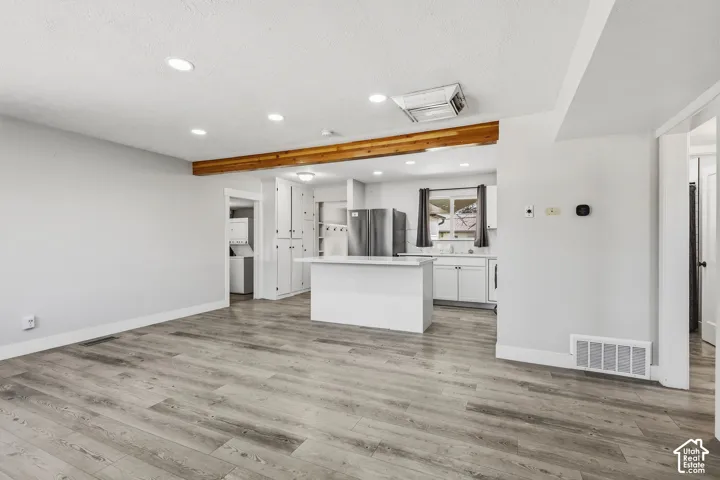 Wood-finish flooring throughout, recessed lighting, exposed wood beam, white shaker cabinetry, and a kitchen island