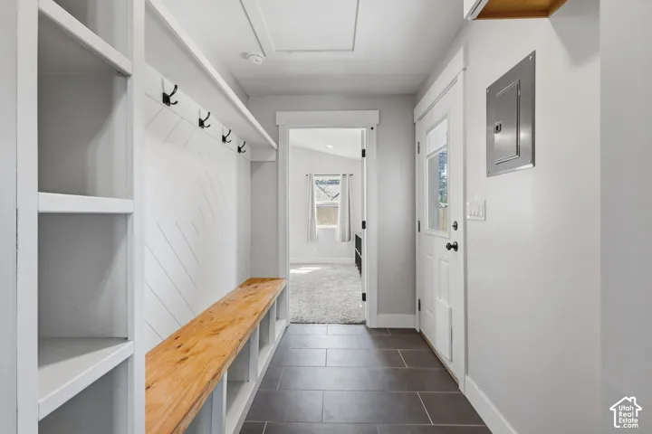 Built-in shelving with coat hooks, natural wood-finish bench seating, white paneled wall accent, and dark tile flooring