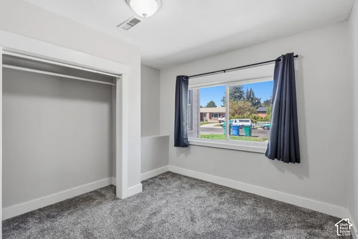 Plush carpet flooring, neutral paint palette, window with curtain rods, and an integrated closet with a hanging rod