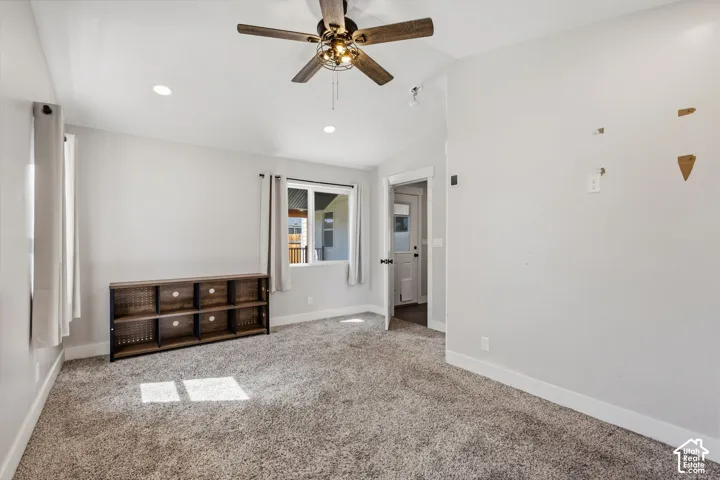 Recessed ceiling lights, ceiling fan with wood-finish blades, light-colored carpeting, two windows, and white trim