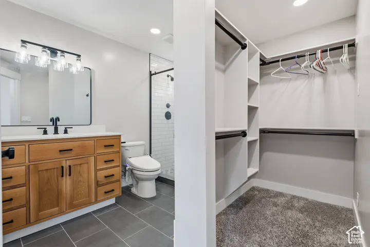Bathroom featuring a wood-finish vanity with a white countertop and matte black fixtures, a walk-in shower with subway tile, and large format floor tile