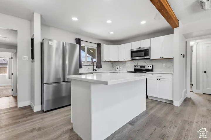 Kitchen featuring a center island with a solid surface countertop, white cabinetry, stainless steel appliances, a tile backsplash, and wood-finish flooring