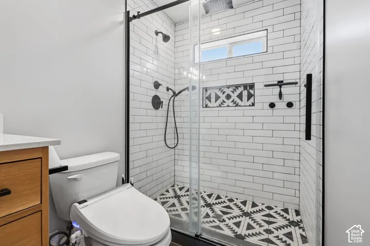 Glass-enclosed shower with matte black hardware, subway tile surround, patterned floor tile, and a built-in niche