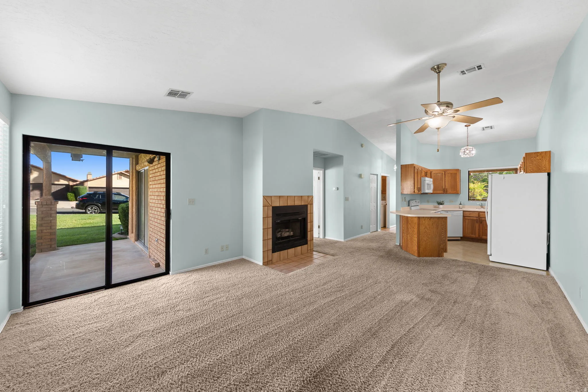 Open-concept living space featuring a fireplace with a brick surround, sliding glass door to an outdoor patio, and a kitchen with wood cabinetry.