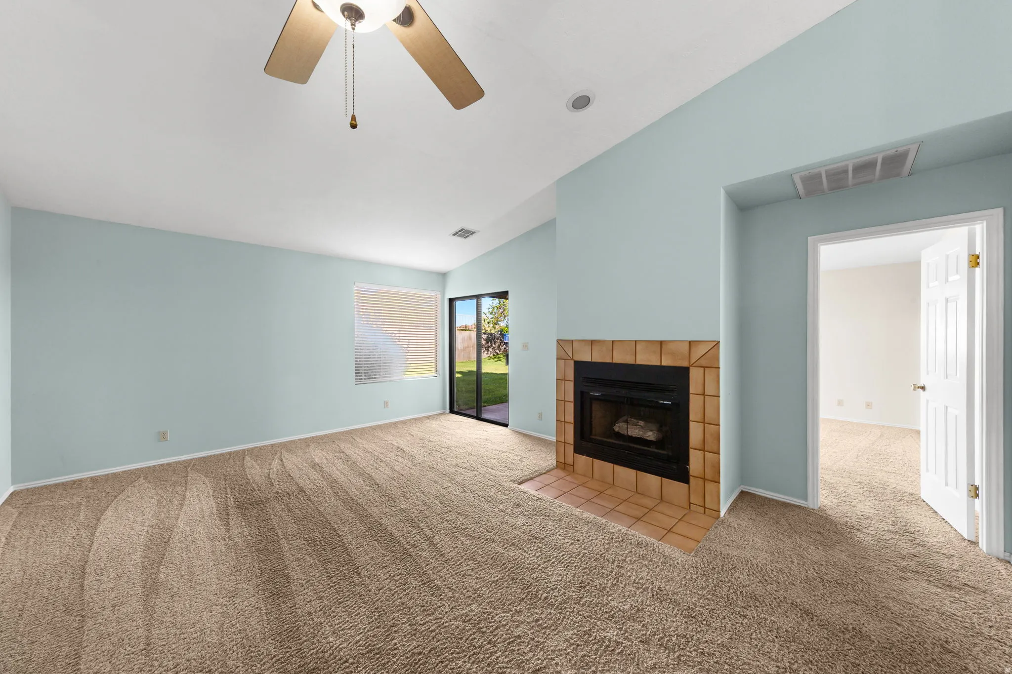 Carpeted living space featuring a tiled fireplace with hearth, ceiling fan, and sliding glass door