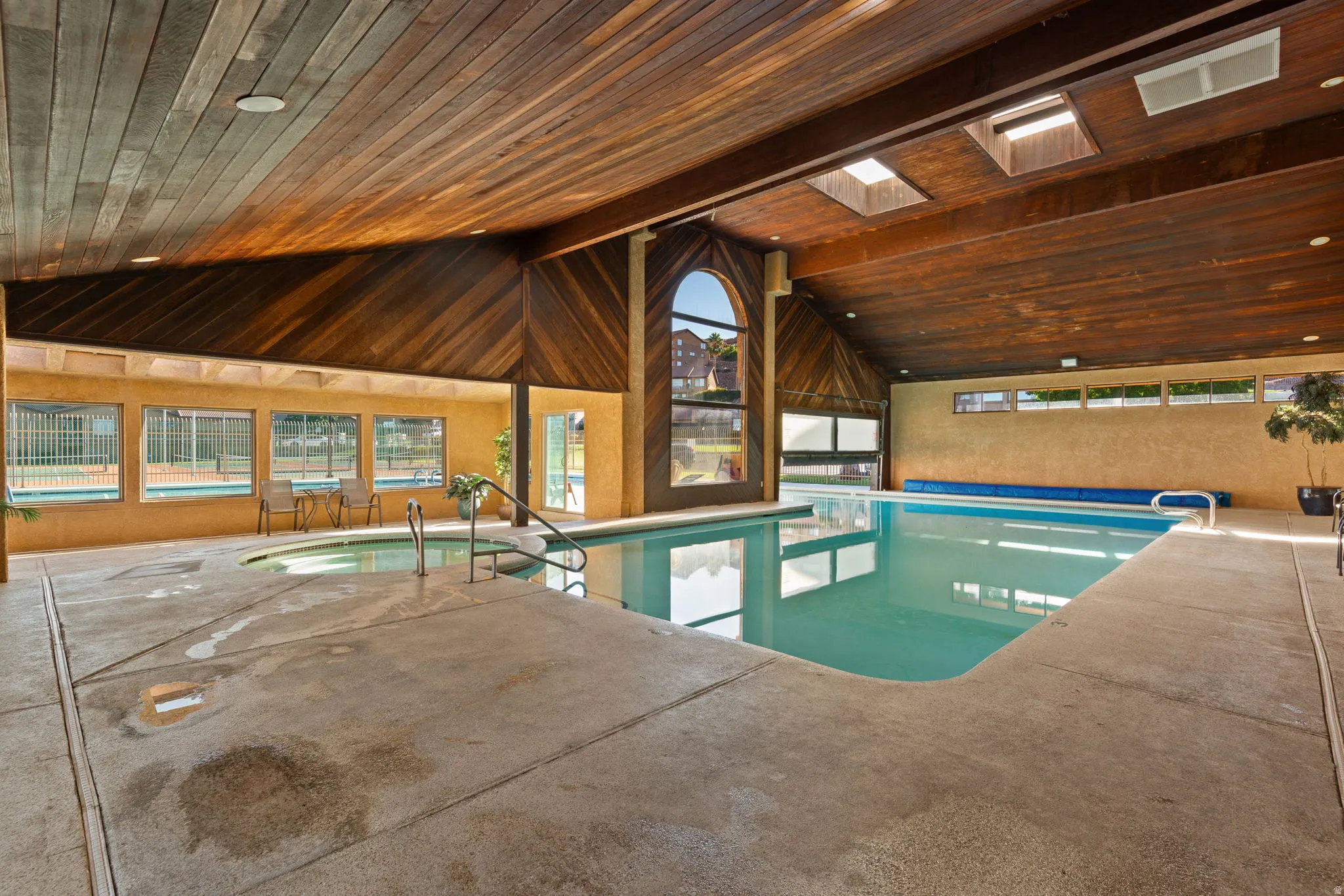 Indoor swimming pool with an integrated spa, wood-paneled vaulted ceiling, and multiple skylights