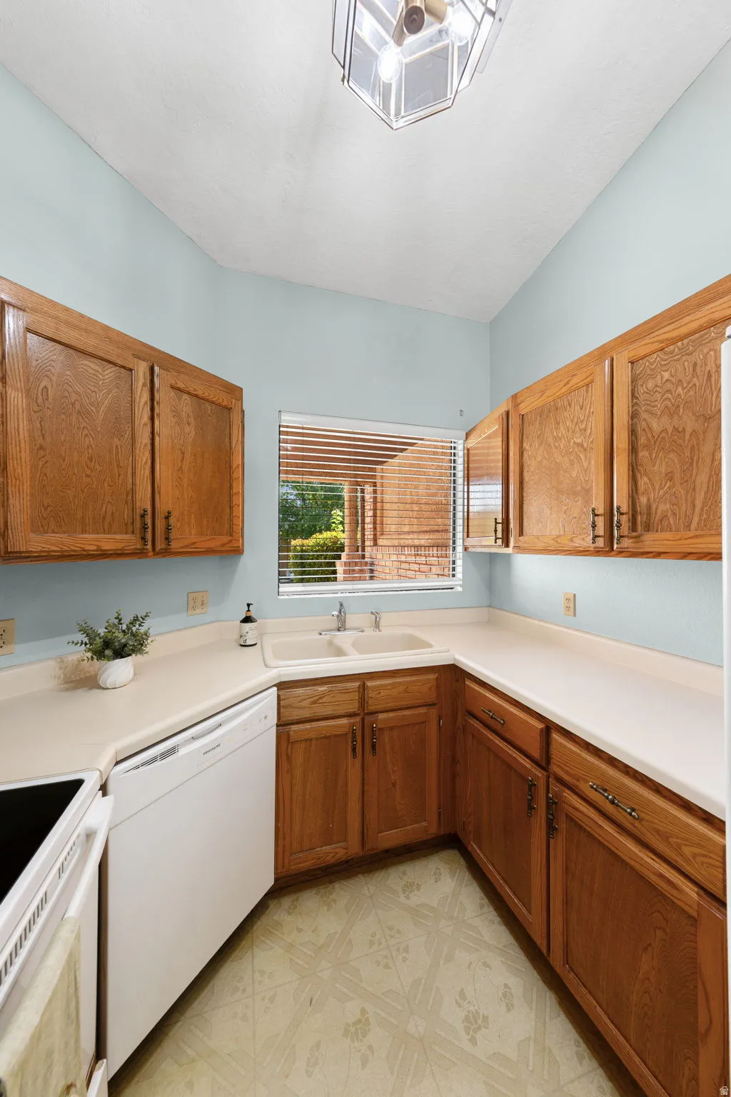 Kitchen featuring wood cabinetry, a double basin sink, white countertops, and a built-in dishwasher