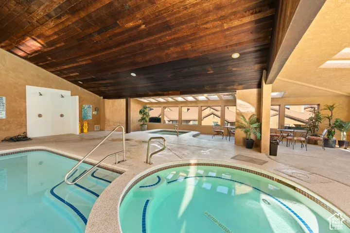 Indoor pool with integrated spa, wood-finish ceiling, and multiple skylights